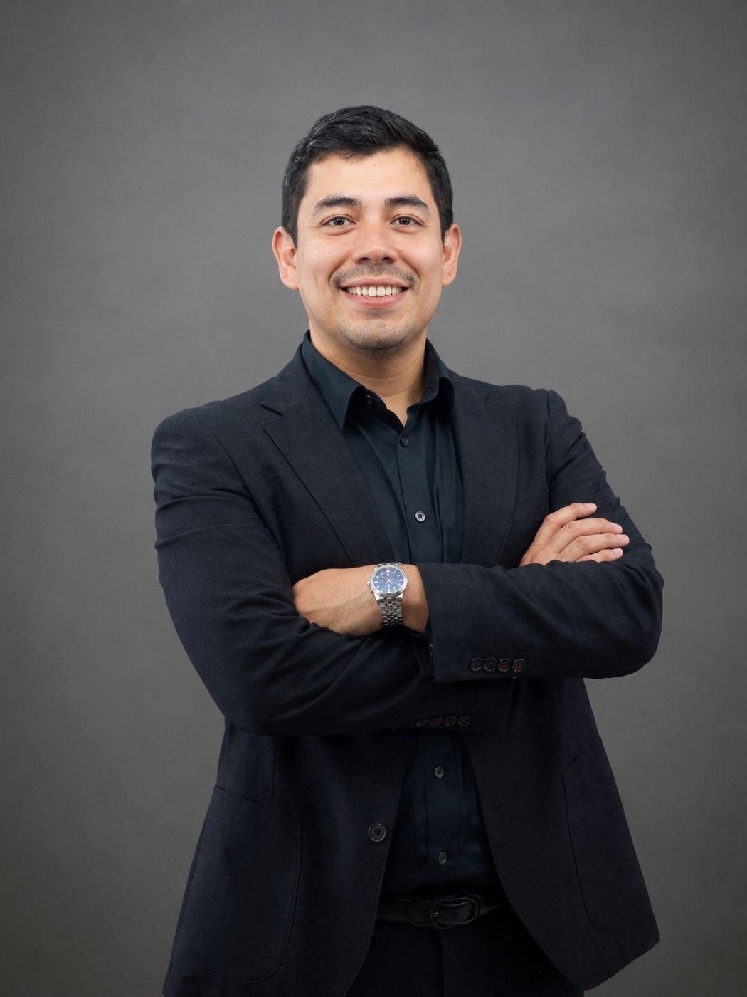 Samuel García, socio de SinergIA 180°, de pie con los brazos cruzados, saco y camisa oscuros, sonriendo a la cámara.